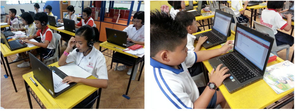 Young students in uniforms sit at yellow desks using laptops in a classroom setting.
